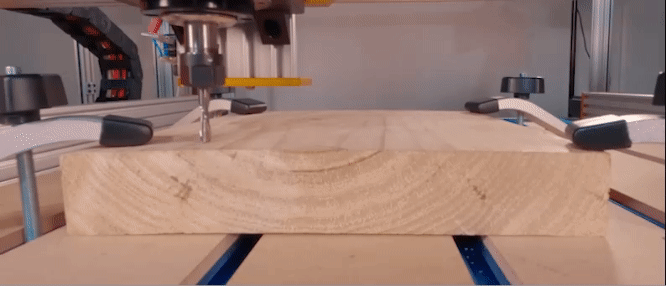 CNC machine conducting a test cut on a slab of wood clamped down using T-Track based spoiler board
